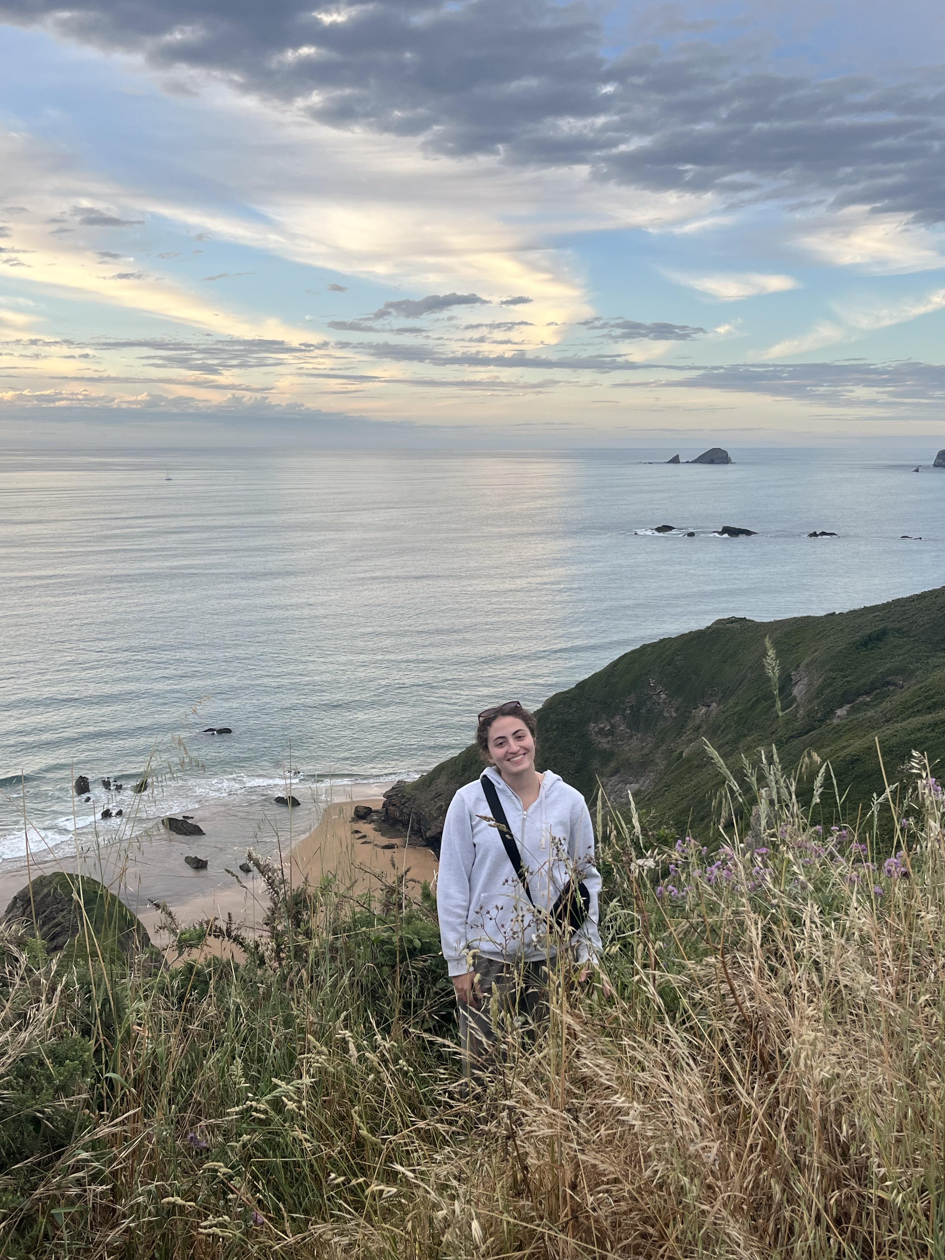 nora standing in tall grass on a clifftop above the sea at sunset